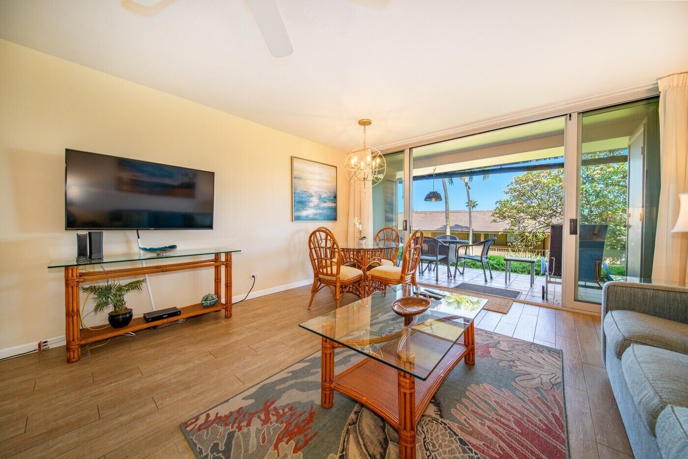A living room with a TV, glass coffee table, wicker chairs, and a view to the outside.