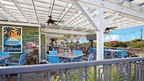 Un área de comedor al aire libre con mesas y sillas, un cartel que dice 'The Cabana Bar & Grill' y vistas del paisaje.