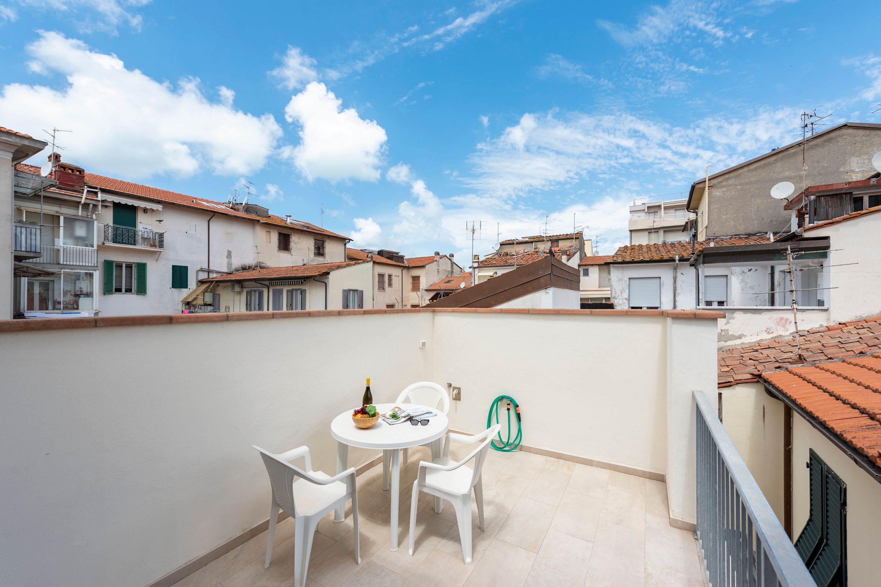 A balcony with a table and chairs, a bottle, and a bowl of fruit.