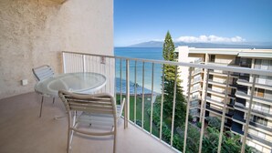 A balcony with a glass table and chairs, overlooking a clear blue sea and a distant mountain.