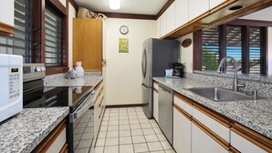 A compact kitchen with a microwave, oven, refrigerator, sink, and wooden cabinets. - Kiahuna Plantation Resort Partial Ocean 2 Bedroom (Koloa)