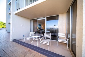Un balcon extérieur avec une table et des chaises, une porte-fenêtre coulissante et une vue sur l’océan.
