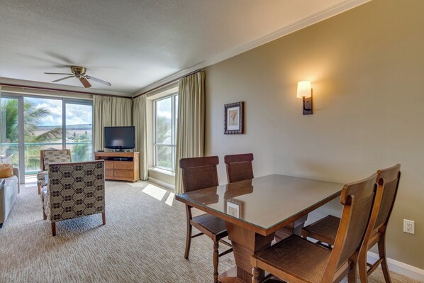 A hotel room with a dining table, chairs, a TV, and a balcony with curtains.