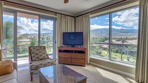 A spacious room with a large TV on a wooden cabinet, a glass coffee table, and a patterned armchair. - Honua Kai Resort View 2 Bedroom (Lahaina)