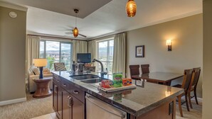 A modern kitchen with a central island, a dining area with two chairs, a ceiling fan, and a large window offering a view. - Honua Kai Resort View 2 Bedroom (Lahaina)