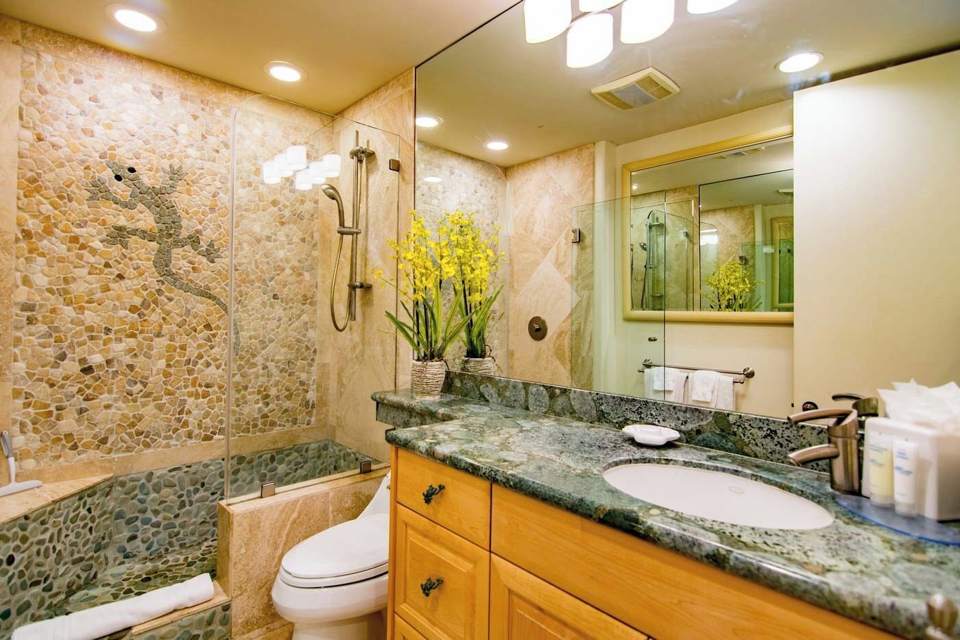 A bathroom with a mosaic wall, a shower, a toilet, a sink, and a vanity.