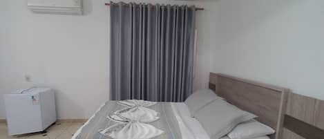 Un dormitorio con cama, mesita de noche, aire acondicionado de pared y luz de techo.