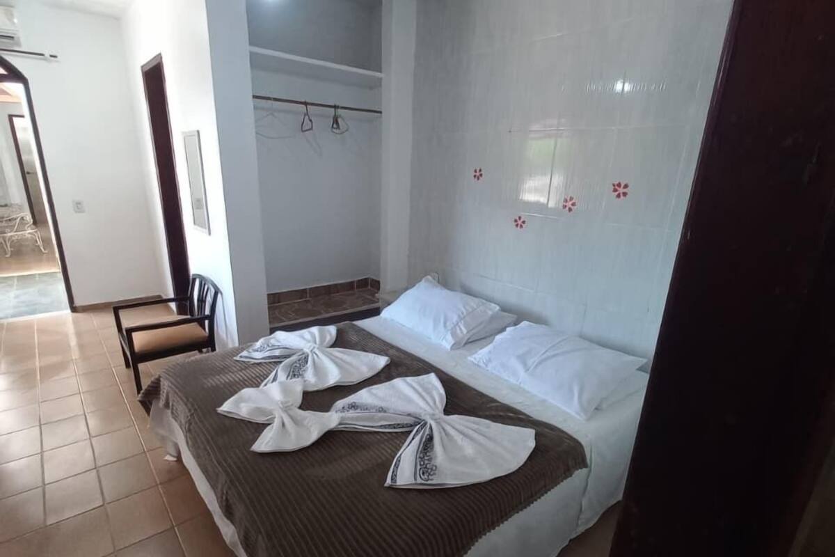 Une chambre d’hôtel avec un lit, un ventilateur de plafond, une armoire et une salle de bain visible à travers une porte ouverte.
