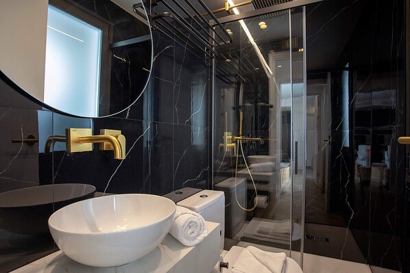 Une salle de bain moderne avec un grand lavabo blanc, un robinet doré et une douche séparée par des parois en verre.