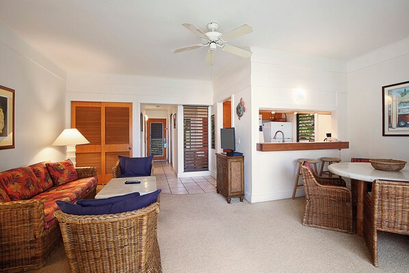 A living room with a sofa, a TV, a dining area with a table and chairs, and a kitchen area with a fridge and counter.