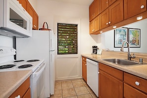 A compact kitchen with a stove, refrigerator, dishwasher, and a window with blinds.