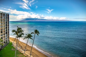 A beachfront hotel with a view of the ocean and a mountain in the distance.