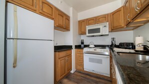 Eine Küche mit Holzausstattung, einem weißen Kühlschrank, einer Mikrowelle, einem Herd und einem Spülbecken.