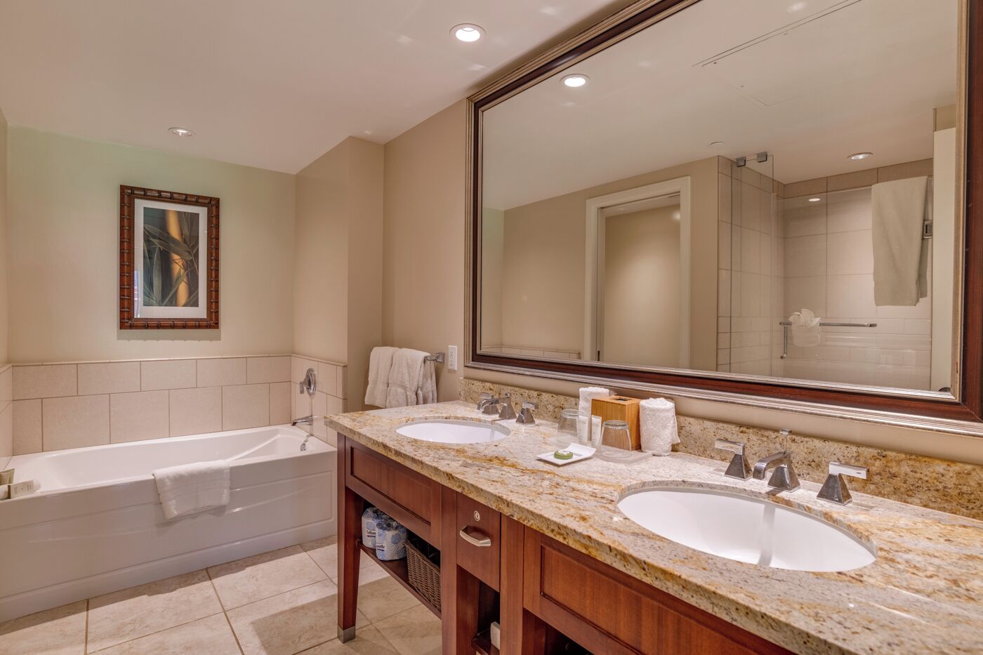 Une salle de bain avec une baignoire, deux lavabos, un grand miroir et un tableau encadré au mur.