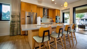 A modern kitchen with wooden cabinets, a stainless steel refrigerator, a central island with bar stools, and pendant lighting.