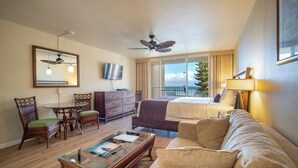 Une chambre d’hôtel comprenant un lit, un canapé, une table basse, une télévision, un ventilateur de plafond, une fenêtre avec vue et une commode.