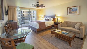 Une chambre d’hôtel avec un lit, un canapé, une table en verre, une chaise, un ventilateur de plafond et un balcon avec vue.
