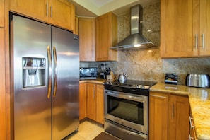 A kitchen with stainless steel appliances, wooden cabinets, granite countertops, and a stainless steel range hood.