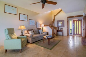 A living room with a sofa, armchair, coffee table, and a ceiling fan.
