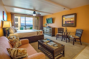 A hotel room with a bed, a sofa, a coffee table, a TV, and a balcony with a view.