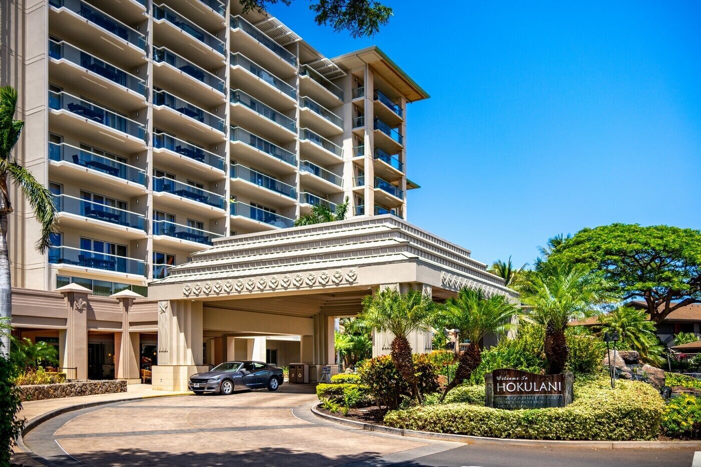 A multi-story hotel with a central entrance, palm trees, and a sign reading "Welcome to HOKULANI."