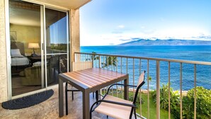 Un balcon avec une table et des chaises, donnant sur un plan d’eau et des montagnes.