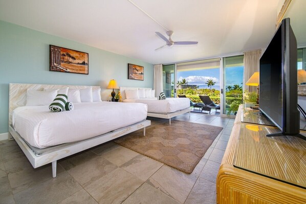A hotel room with two beds, a television, a ceiling fan, and a view of the ocean.