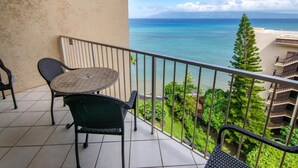 Un balcon avec une table et des chaises, offrant une vue sur la côte, avec de la verdure et une montagne lointaine.