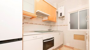 Una cocina con armarios blancos, un horno, un lavamanos y un ventanal con puerta de vidrio esmerilado.
