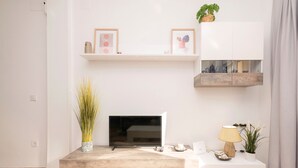 Una sala de estar moderna con un televisor de pantalla plana, una mesa de centro, una lámpara y objetos decorativos en estanterías.