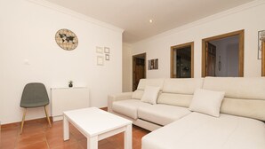 A living room with a white sofa, a small table, and a chair. There is a world map on the wall and a picture frame. - El Cortijo in La Linea de la Conception (La Línea de la Concepción)