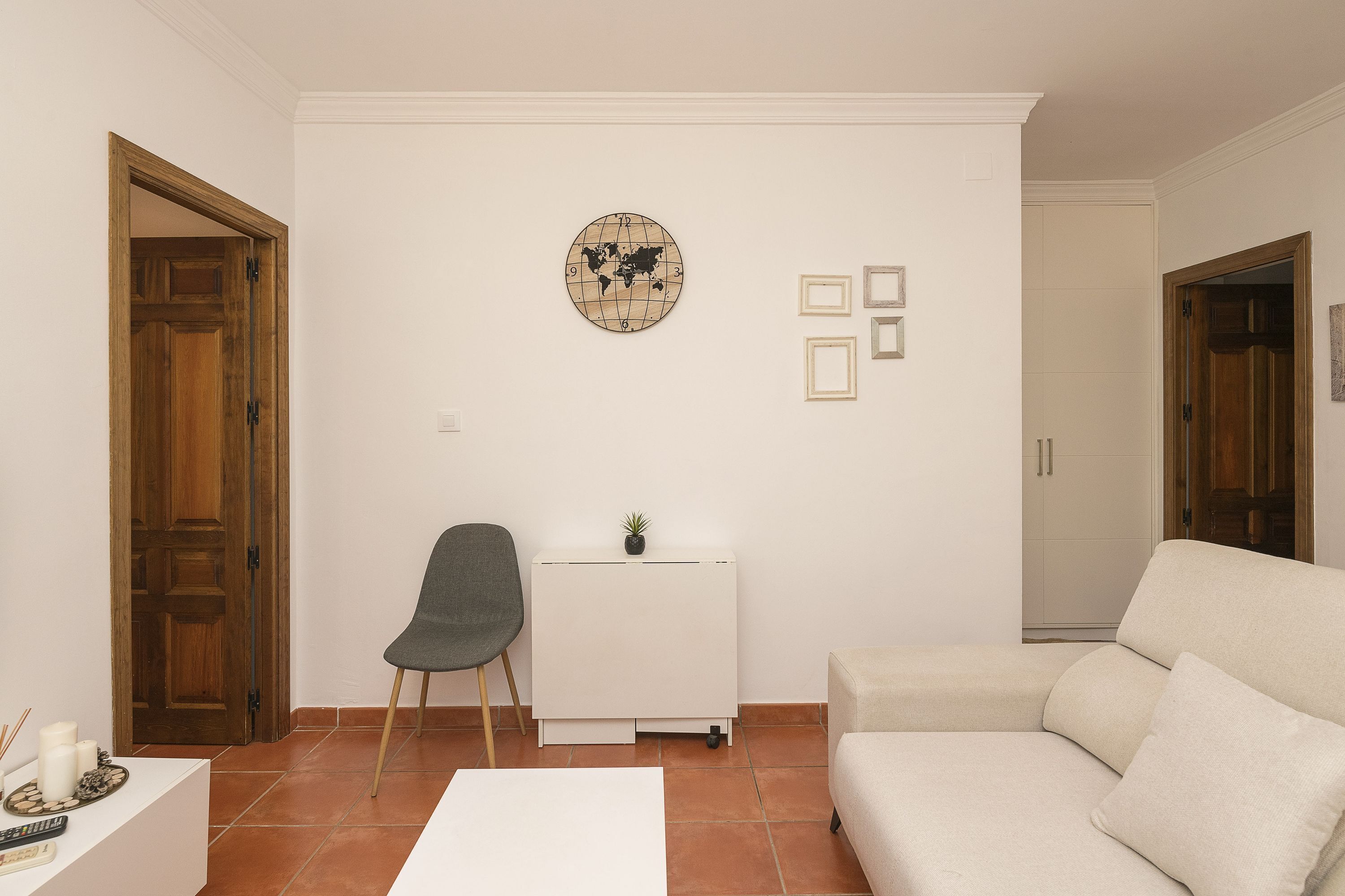 Un salon avec un canapé blanc, un fauteuil gris, un petit meuble blanc orné d’une plante et une carte du monde accrochée au mur.