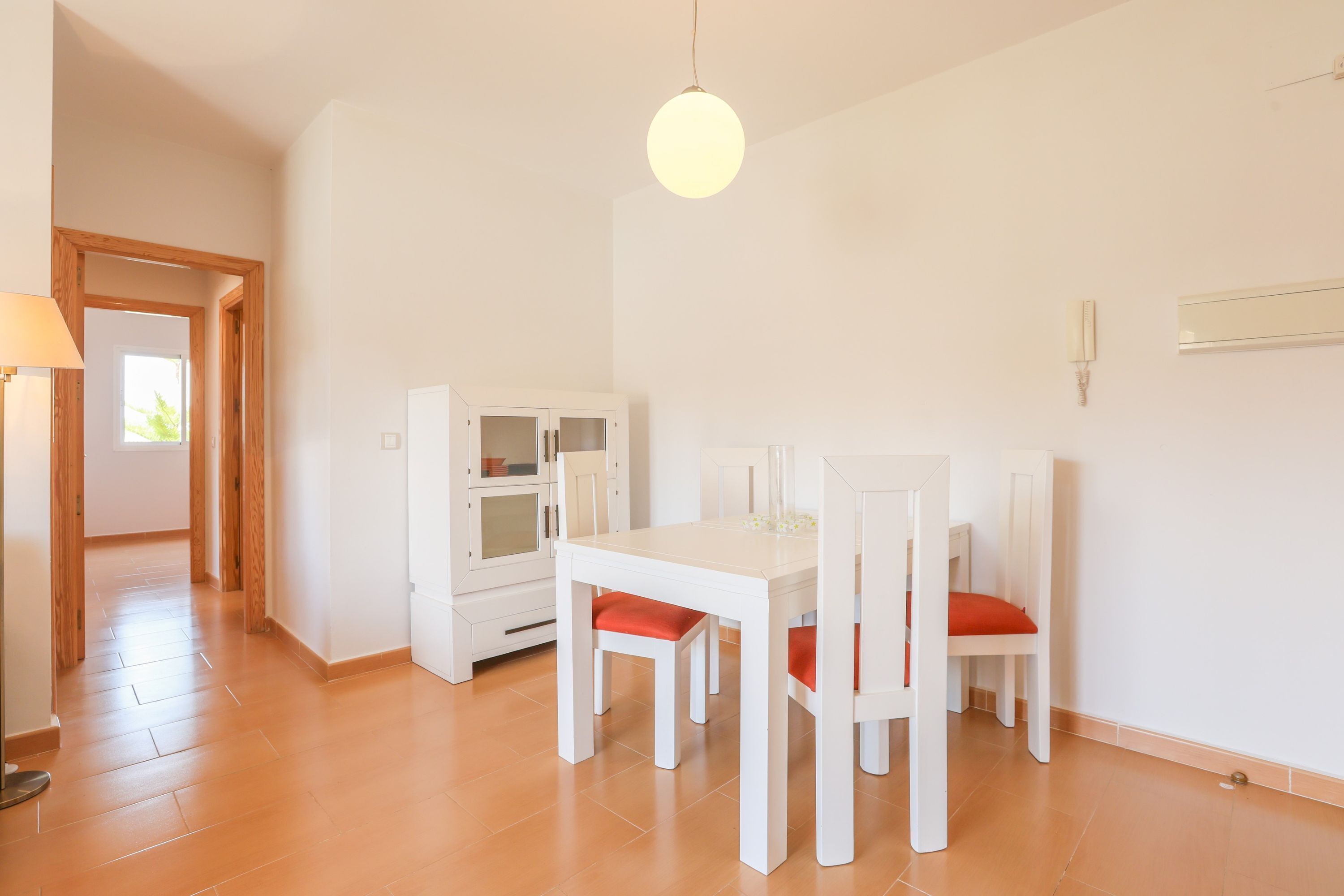 A dining area with a white table and chairs, a hanging light fixture, and a cabinet with glass doors.