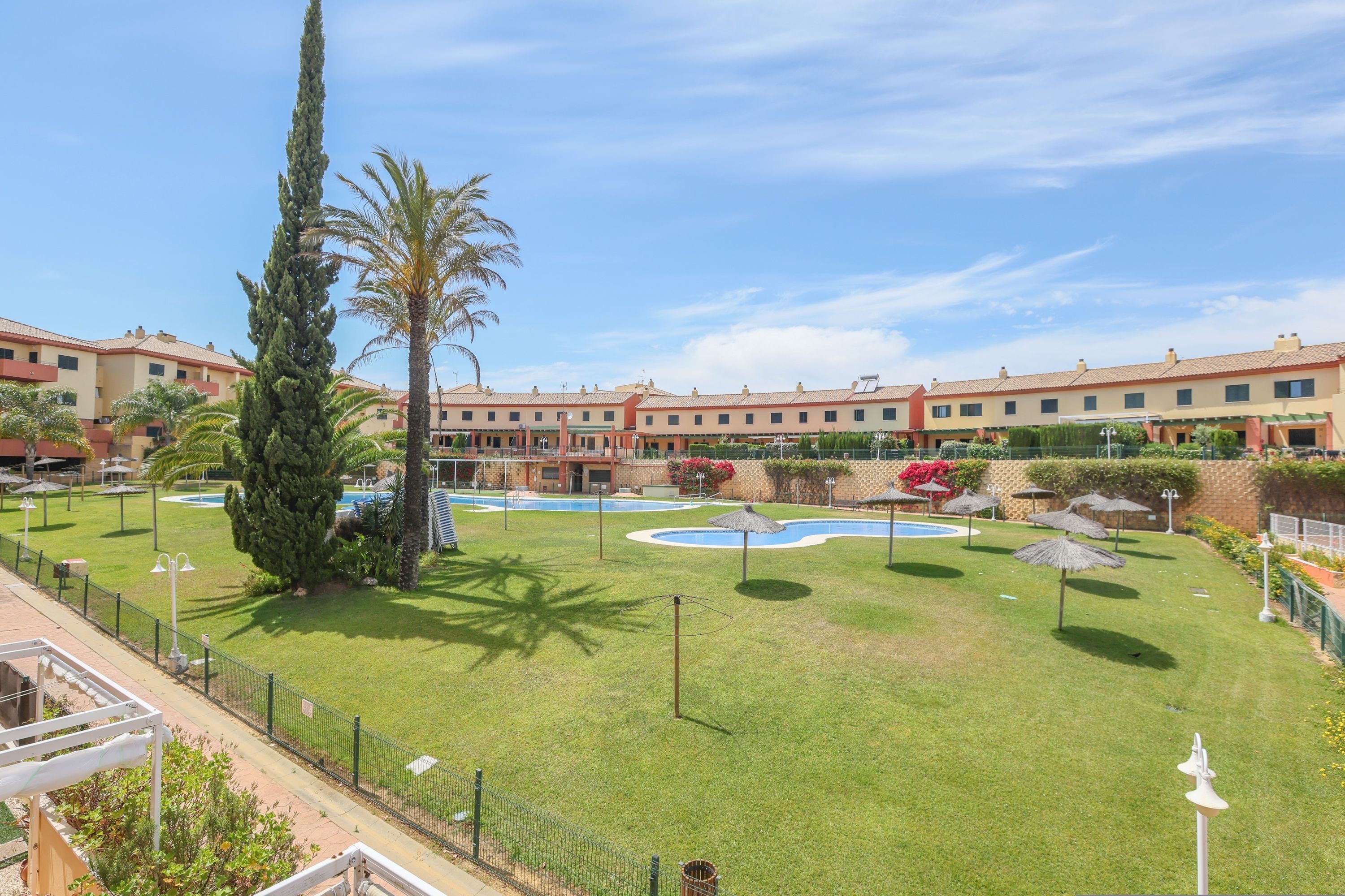 Un patio de hotel con piscina, palmeras y una valla.
