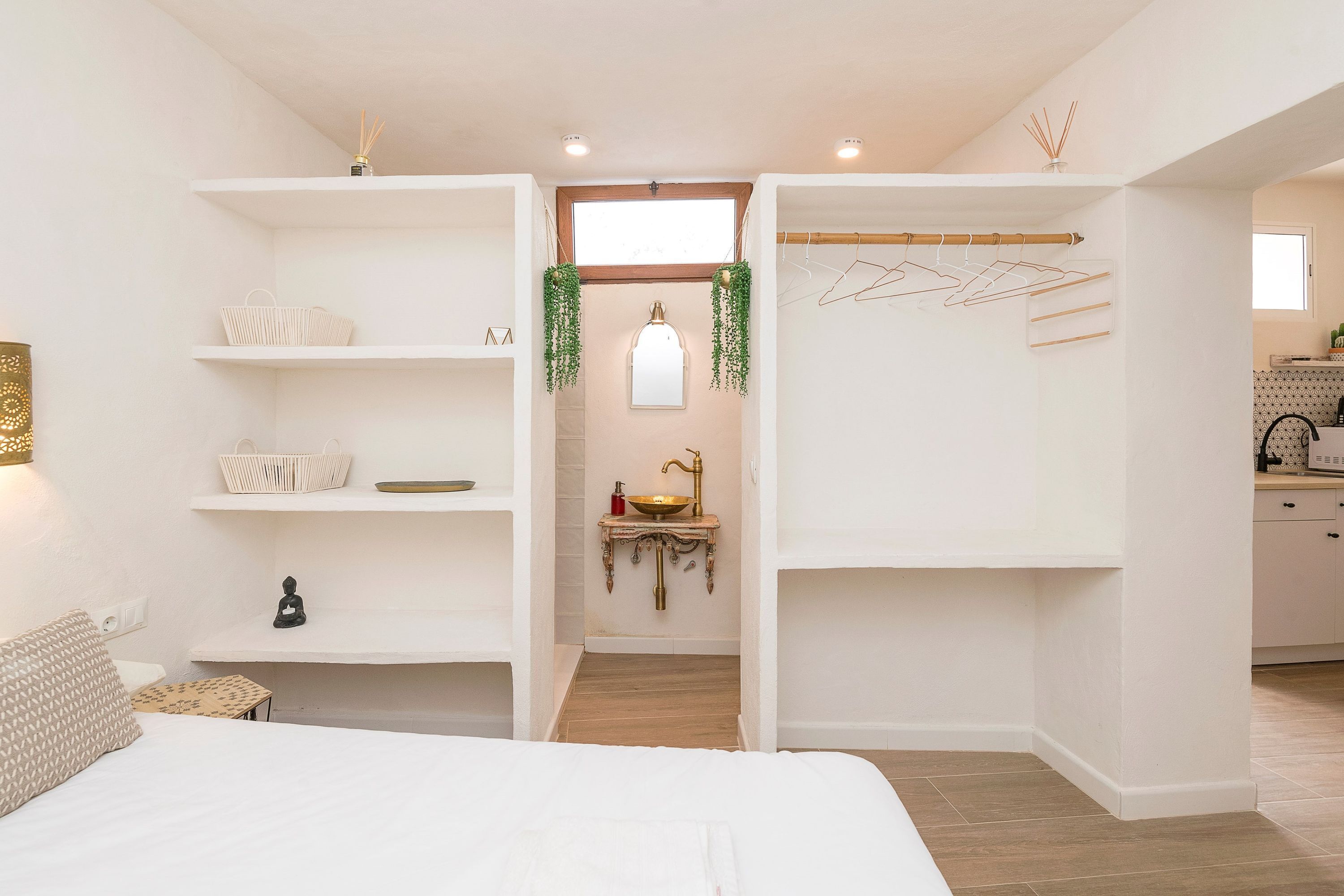 Un dormitorio moderno y bien iluminado, con una cama grande, estanterías empotradas, una mesita de noche pequeña y una planta colgante.
