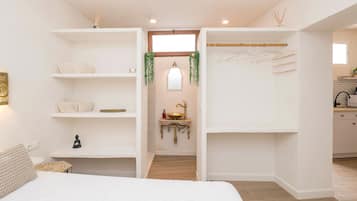 Un dormitorio moderno y bien iluminado, con una cama grande, estanterías empotradas, una mesita de noche pequeña y una planta colgante.