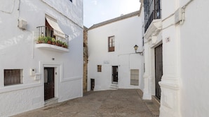A narrow street with white buildings, a door, and a small balcony with potted plants. - Pura Vida in Vejer de la Frontera (Vejer de la Frontera)
