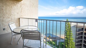 A balcony with a round table and two chairs, overlooking a beach and ocean.