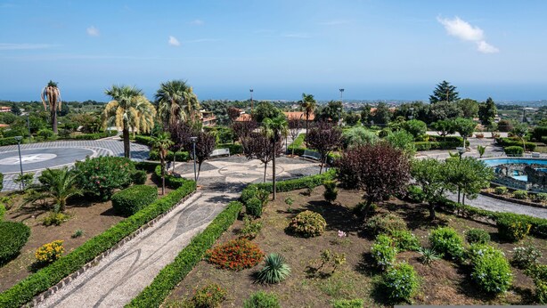 A landscaped garden with a circular driveway, palm trees, and a pool area. - Villa With Volcano View (Zafferana Etnea)