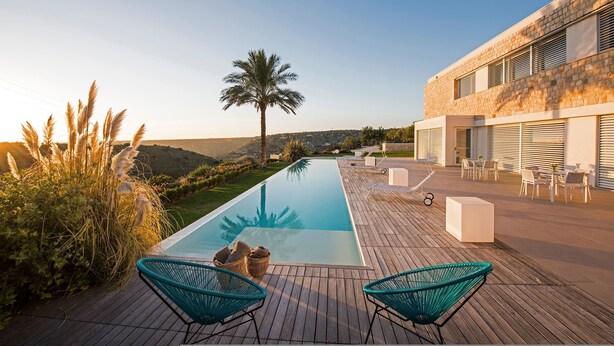 Et moderne poolområde med træterrasse, to grønne stole og et loungeområde med borde og stole.