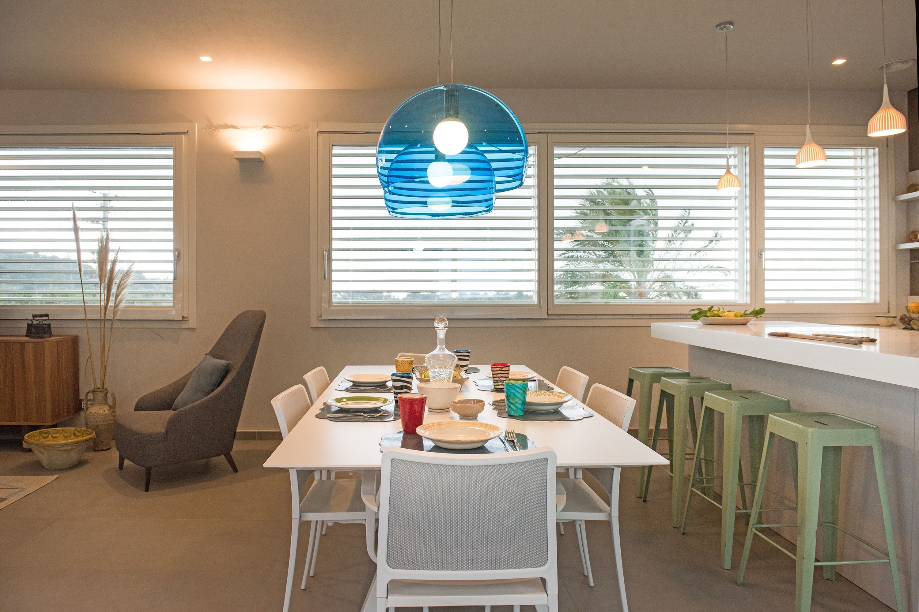 A modern dining area with a white table set for four, surrounded by green bar stools.