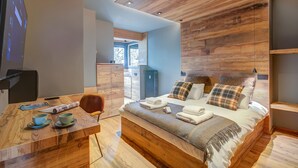 A modern bedroom with a wooden ceiling, a large bed with multiple pillows, a bedside table with cups and a magazine, and a view of a balcony. - Simona Luxuryapartment few Steps From ski (Sestriere)