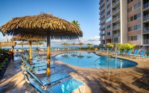 A poolside area with lounge chairs, a pool, and a building in the background.