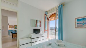 Habitación de hotel con cama, televisor en una cómoda, balcón con vistas y un cuadro en la pared.