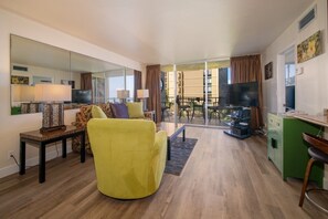 En moderne stue med sofa, fjernsyn, spiseplads og balkon med udsigt.