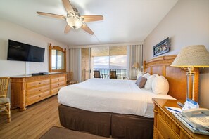 Une chambre d’hôtel avec un grand lit, un ventilateur de plafond, une télévision, une commode en bois et un balcon avec vue.