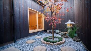 Un jardín japonés tradicional con una construcción de madera, un farol y un árbol con hojas otoñales.
