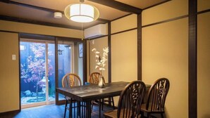 A dining area with a table and chairs, a vase with flowers, and a view of a garden through a glass door. - Kyomachi Rakunan (Kyoto)