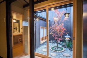 Un intérieur japonais traditionnel avec des portes coulissantes, un petit jardin agrémenté d’un cerisier et un chemin de pierres.
