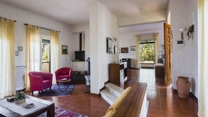 A spacious living area with a sofa, armchair, and coffee table. A kitchen with a stove and cabinets is visible in the background. - Pedara Escape With Garden by Wonderful Italy (Pedara)